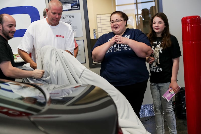 Darlene Lefevre and her daughter, Sophia, 10, watch as the cover is pulled off a 2015 Chrysler 200 that was donated to them at Higgins Body and Paint in West Valley City on Wednesday, June 27, 2018. Geico and Higgins Body and Paint, along with other organ