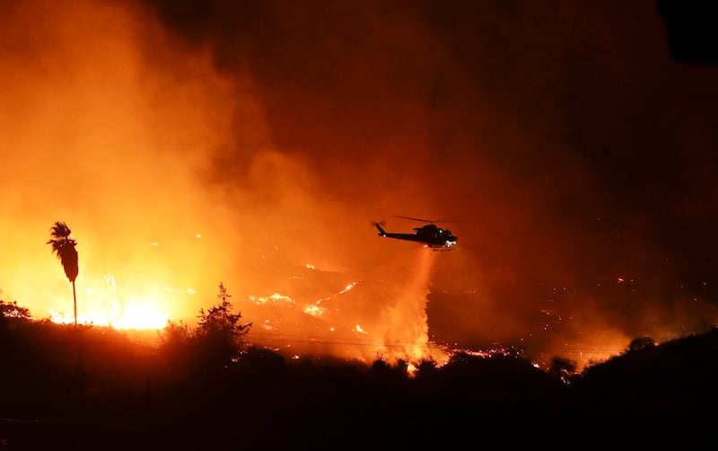 A helicopter drops water over a wildfire Thursday, Dec. 7, 2017, in Bonsall, Calif. The wind-swept blazes have forced tens of thousands of evacuations and destroyed dozens of homes in Southern California.