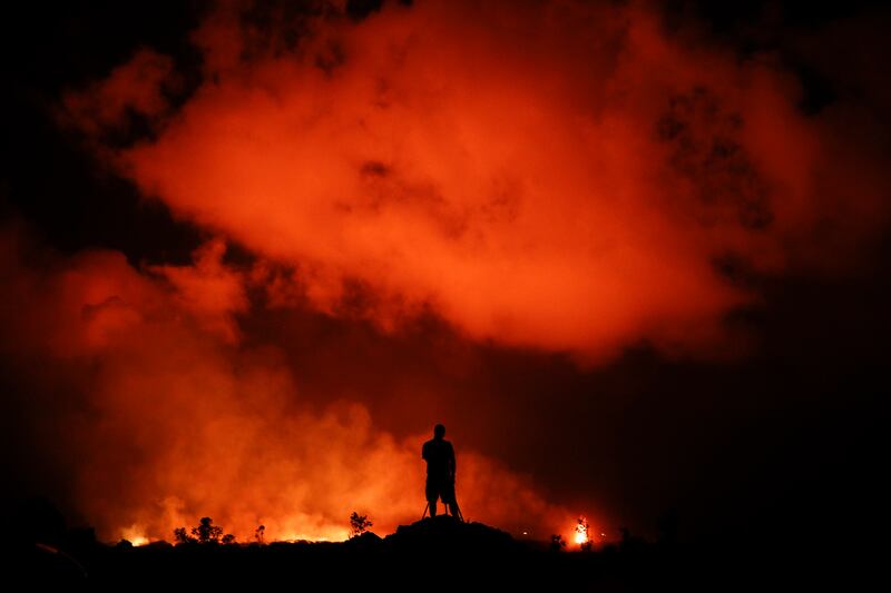 FILE - In this Friday, May 18, 2018 file photo, Peter Vance photographs lava erupting in the Leilani Estates subdivision near Pahoa, Hawaii. A year after one of Kilauea volcano’s largest and most destructive eruptions, people who lost their Big Island hom
