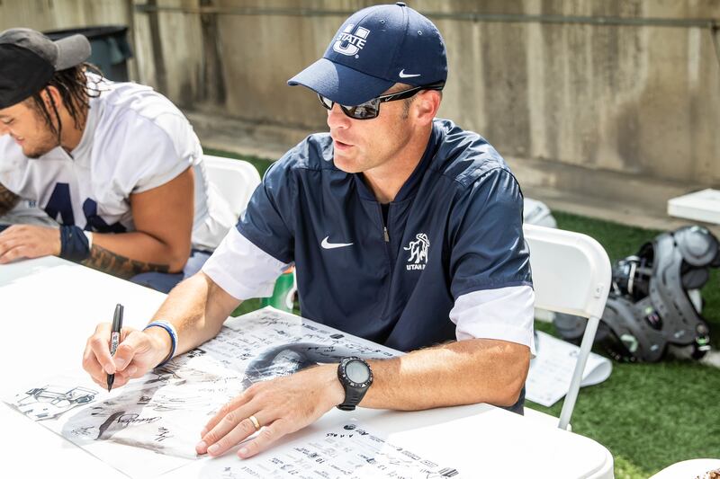 Sixth-year Utah State head coach Matt Wells signs an autograph after the Aggies' third scrimmage of fall camp on Saturday, Aug. 18, at Maverik Stadium in Logan, Utah.