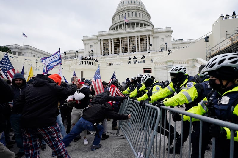 Trump supporters holding Trump flags and American flags push against a metal barrier with police officers on the other side pushing back.