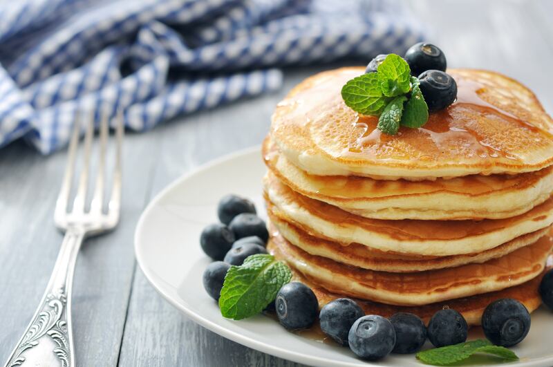 Pancakes with blueberries around them on a white plate with a fork next to it.