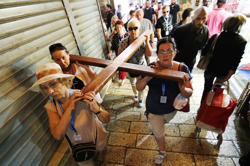 Pilgrims carry a cross during Stations of the Cross in the Old City market in Jerusalem on Friday, April 13, 2018.
