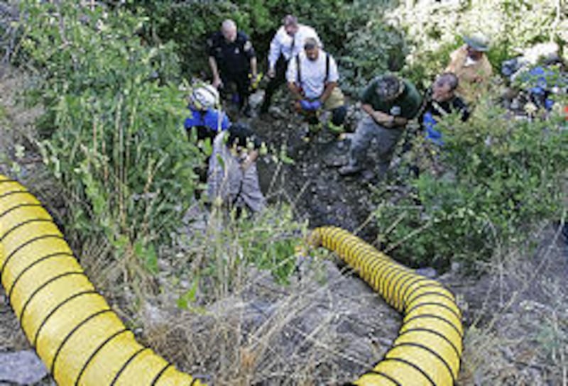 An air hose winds down the hill as search and rescue personnel gather at the mouth of a small cave in Provo where four people died on Thursday in a caving accident. Authorities are sealing the cave's entrance.
