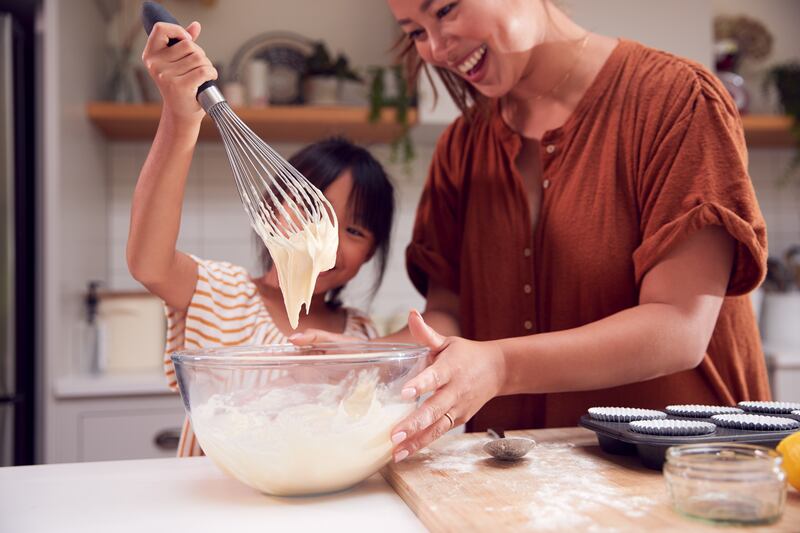 A daughter and mother spend quality time baking muffins together in their kitchen at home.