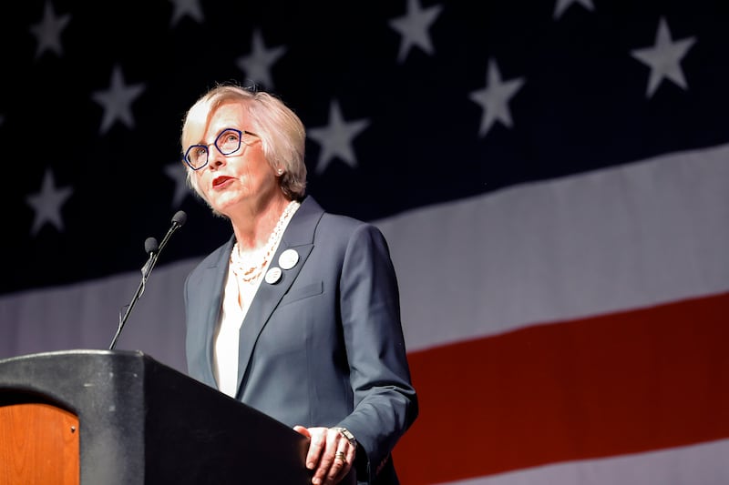 Becky Edwards stands at a podium in front of an American Flag and speaks.
