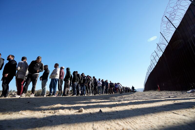 Men line up to receive food from volunteers after crossing the U.S. border with Mexico on Oct. 24, 2023, near Jacumba, Calif.