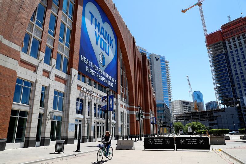 A person on a bike rides past a large banner hanging outside American Airlines Center, home of the Dallas Mavericks and the Dallas Stars, in Dallas, Thursday, April 16, 2020. The banner, which has a Mavericks logo on it, thanks first responders and healthcare workers during the COVID-19 crisis. (AP Photo/Tony Gutierrez)