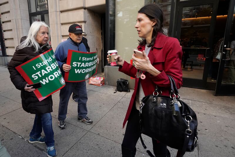 Isabel Johnston, left, and John Papandrea carry signs supporting Starbucks workers outside a Starbucks on New York’s Upper West Side on Nov. 16, 2023.