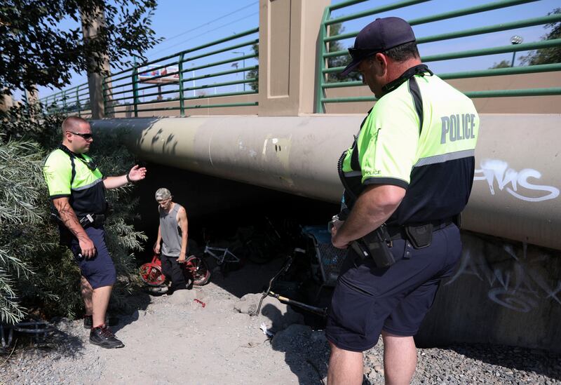 Salt Lake City police officer Austin Gold motions for some people to come out from under a bridge by the Jordan River while patrolling with officer Chuck McNamee in Salt Lake City on Tuesday, Aug. 14, 2018.