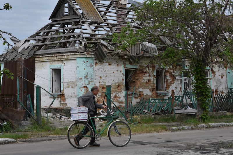 A local man hauls a bicycle with humanitarian aid in front of a house which was destroyed by Russian shelling in Orihiv, Ukraine, on Monday, May 22, 2023.