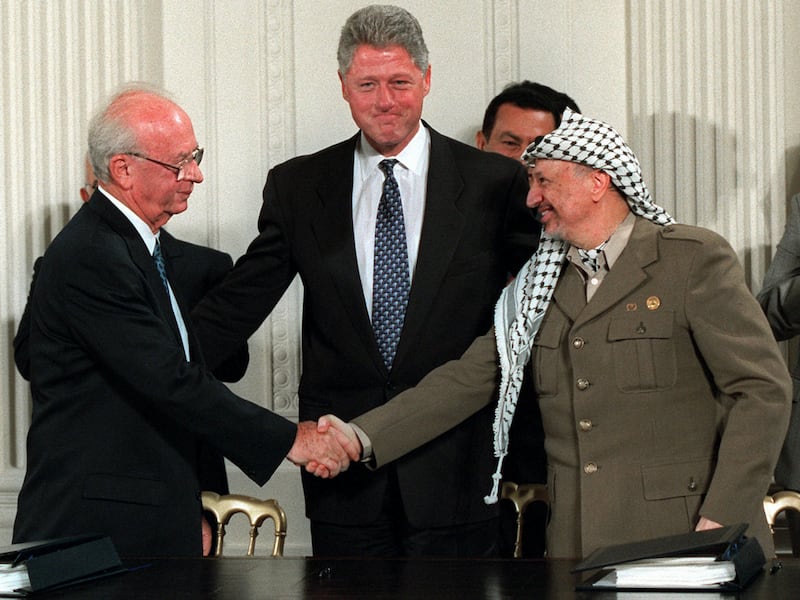 President Bill Clinton gestures toward Israeli Prime Minister Yitzhak Rabin, left, and PLO leader Yasser Arafat shaking hands in the East Room of the White House after the Mideast accord signing on Sept. 28, 1995.