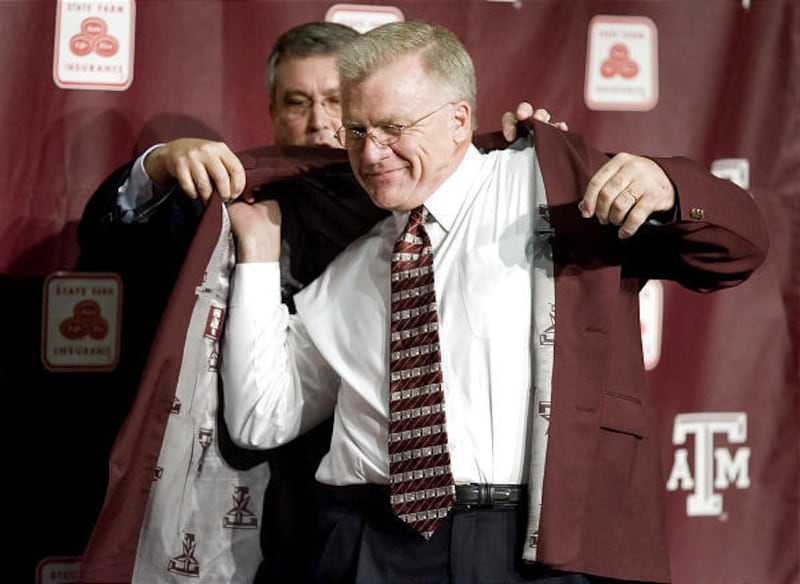 New Texas A&M football coach Mike Sherman gets a hand putting on his maroon jacket.