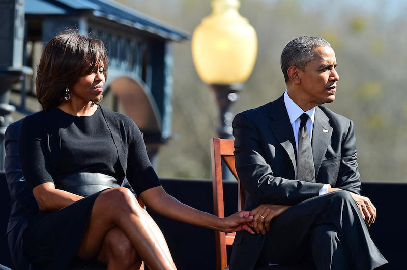 First lady Michelle Obama holds the hand of her husband President Barack Obama as U.S. Rep. John Lewis, D-Ga., speaks before a symbolic walk across the Edmund Pettus Bridge, Saturday, March 7, 2015, in Selma, Ala. This weekend marks the 50th anniversary o