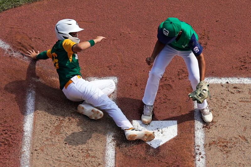 Davenport, Iowa’s Jameson Andresen, left, scores on a wild pitch by Major Rodarte of Bonney Lake, Wash., right, during the first inning of a game at the Little League World Series. The game was not without controversy.