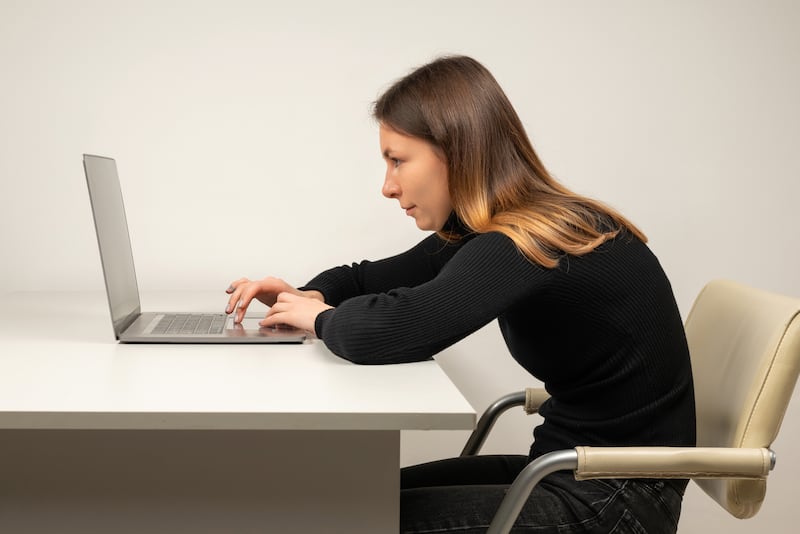 A woman slouches at a desk while typing on a computer.