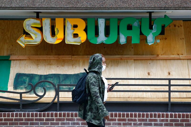 A woman wears a face mask near a Subway restaurant sign.