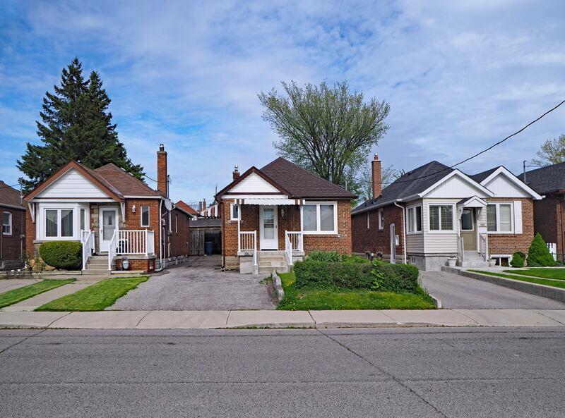 Three small houses sit on an empty street with trees and green lawns.