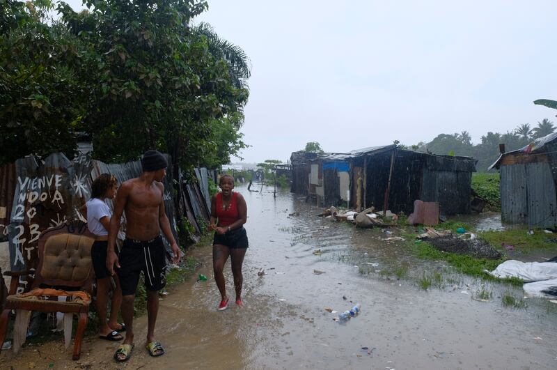 People walk between houses flooded by the rains of Tropical Storm Franklin, along the Ozama River in the Gualey neighborhood of Santo Domingo, Dominican Republic.
