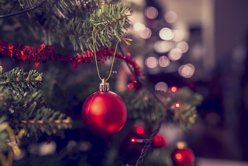Closeup of red bauble hanging from a decorated Christmas tree.