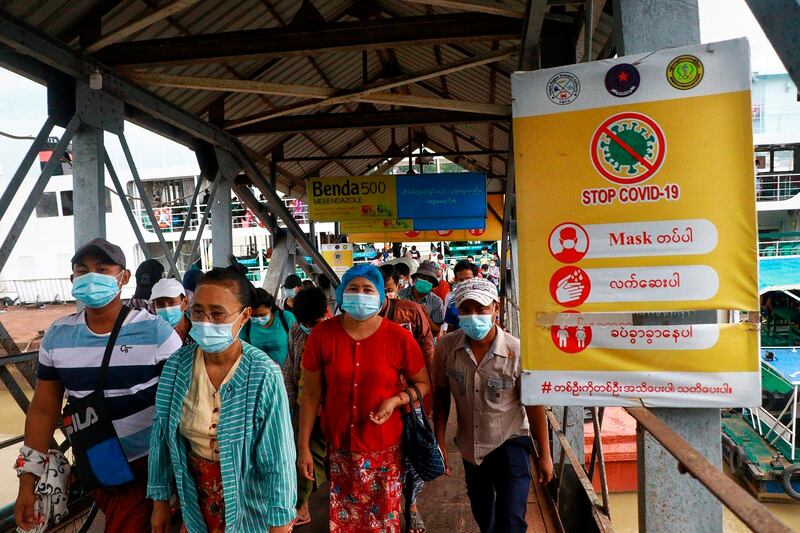 Ferry passengers wearing face masks walk past a “Stop COVID-19” poster at the Pansodan jetty in Yangon, Myanmar.