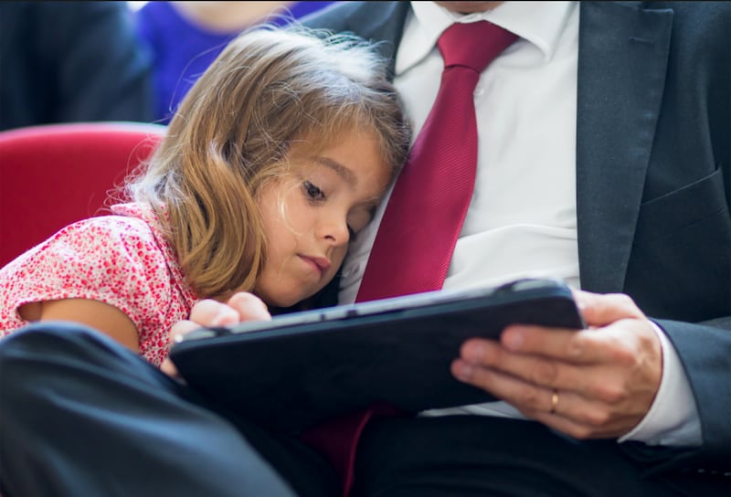 A daughter leans against her father while reading on a tablet.