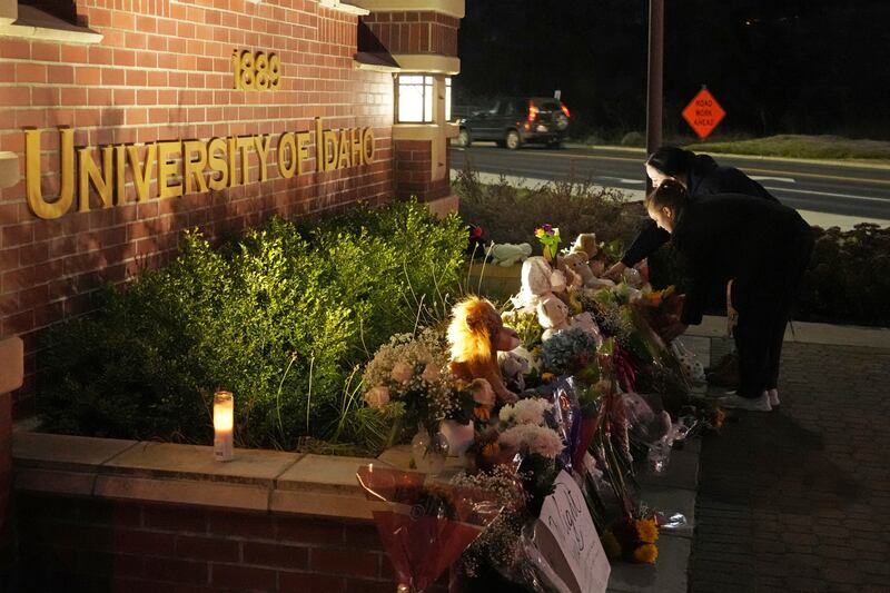 Two people place flowers at a growing memorial in front of a campus entrance sign for the University of Idaho in Moscow, Idaho.