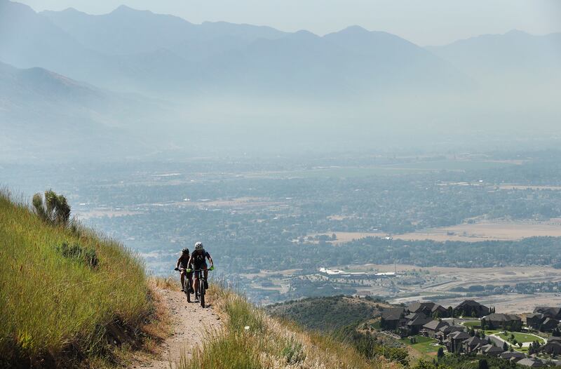 Cyclists ride the Eagle Crest Trail that offers a view of smoke-filled Utah County on Friday, July 6, 2018.