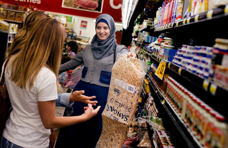 Baraa Huraideen shows sangak, an Iranian flatbread, to Jamie Cook and Lisa Lovell as they shop for groceries at Rancho Market in Millcreek on Sept. 12. The volunteers visit Baraa and her family weekly.