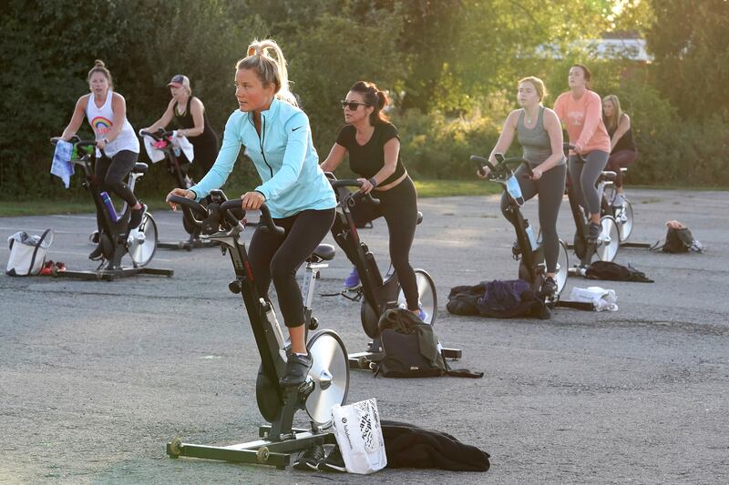 Jackie Brennan pedals on a stationary exercise bike with others during a spinning class in a parking lot outside Fuel Training Studio.