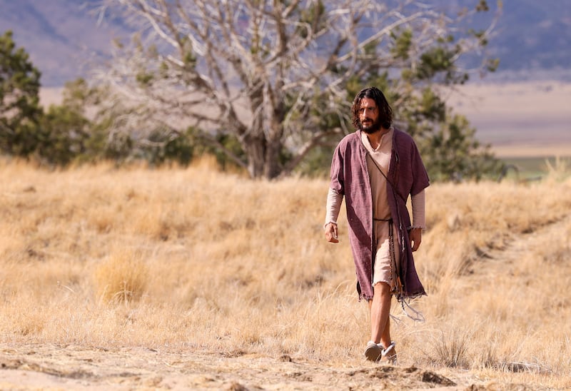 Jonathan Roumie, who plays Jesus, walks toward trailers during filming with mountains in the background.