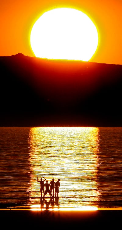 Four visitors to the Great Salt Lake shoreline are framed by the reflection of the setting sun in Salt Lake City, Utah, July 3, 2007.