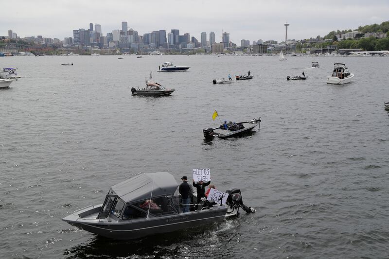 Protesters hold signs that read “Let Us Fish” and “Open State Parks” as they sit on a boat on Lake Union near Gas Works Park in Seattle, Sunday, April 26, 2020, during a protest against Washington state’s current ban on fishing due to stay-at-home orders implemented to prevent the spread of the coronavirus.