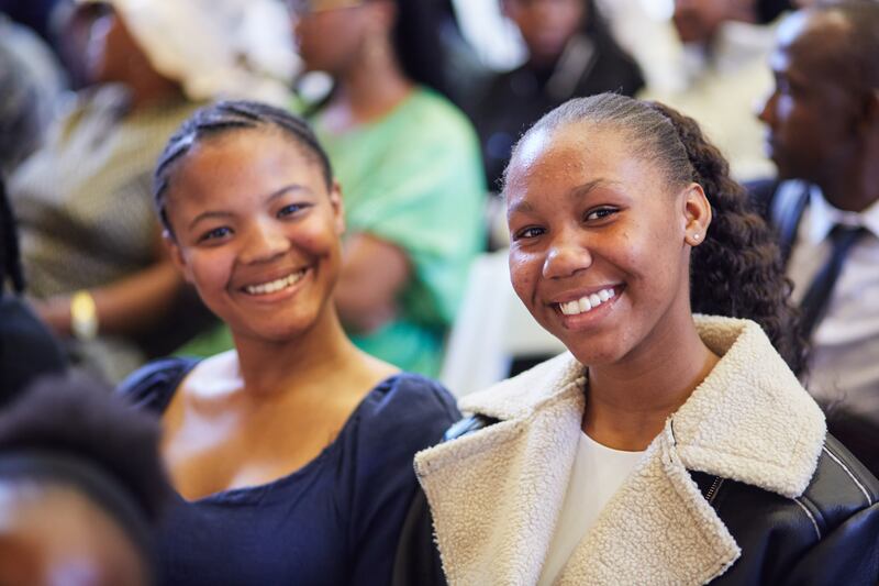 Two young women smile in the congregation during a youth devotional with Elder D. Todd Christofferson in Johannesburg, South Africa.