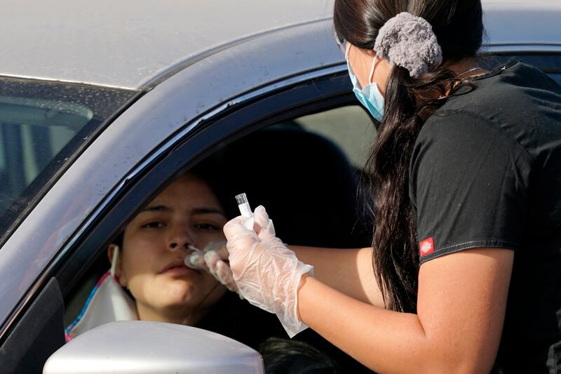 A healthcare worker performs a COVID-19 test at a drive-thru testing center Tuesday, Dec. 8, 2020, in Phoenix.