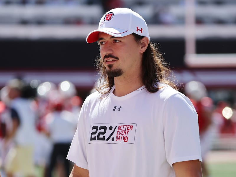Utah Utes quarterback Cameron Rising (wearing white) watches from the sidelines