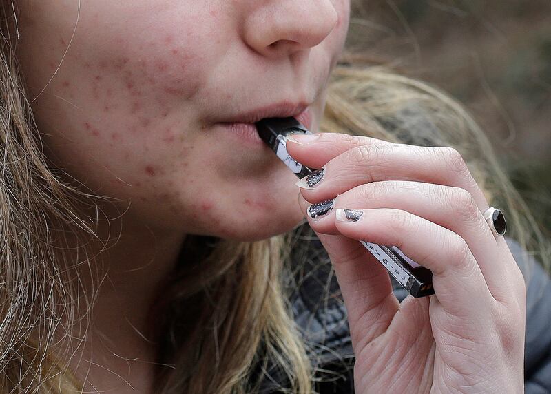 In this April 11, 2018, file photo, a high school student uses a vaping device near a school campus in Cambridge, Mass.