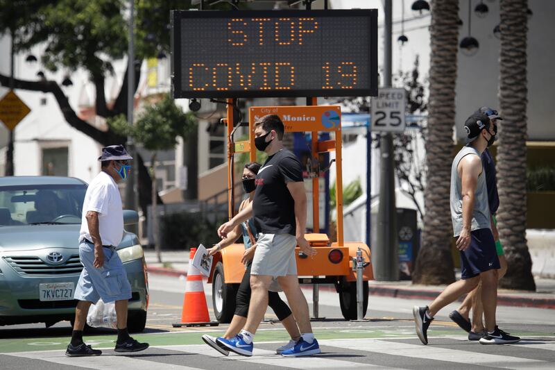 Pedestrians wear masks as they cross a street amid the coronavirus pandemic Sunday, July 12, 2020, in Santa Monica, Calif. A heat wave has brought crowds to California’s beaches as the state grappled with a spike in coronavirus infections and hospitalizations.
