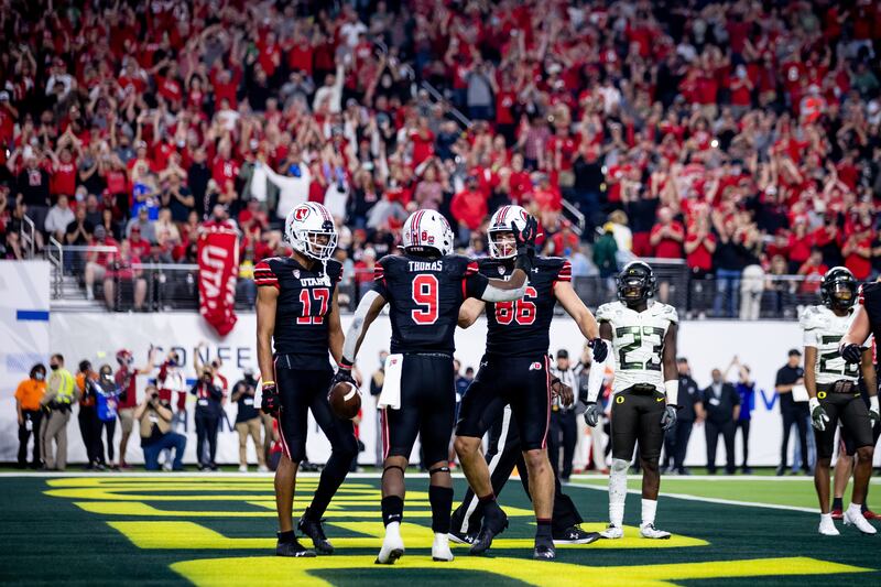 Utah Utes running back Tavion Thomas, wearing black, celebrates with wide receiver Devaughn Vele and tight end Dalton Kincaid