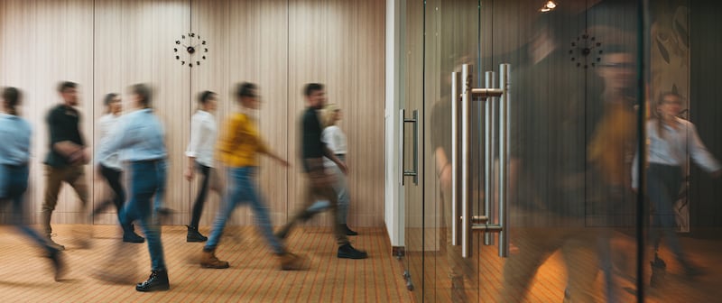 A crowd of employees walks quickly toward the doors of a building.