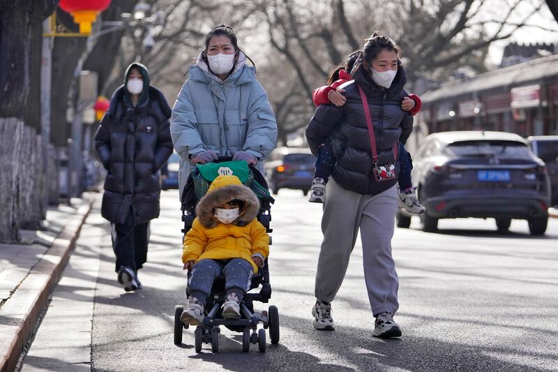 Women wearing face masks walk with their children on a street as they head to Forbidden City in Beijing.