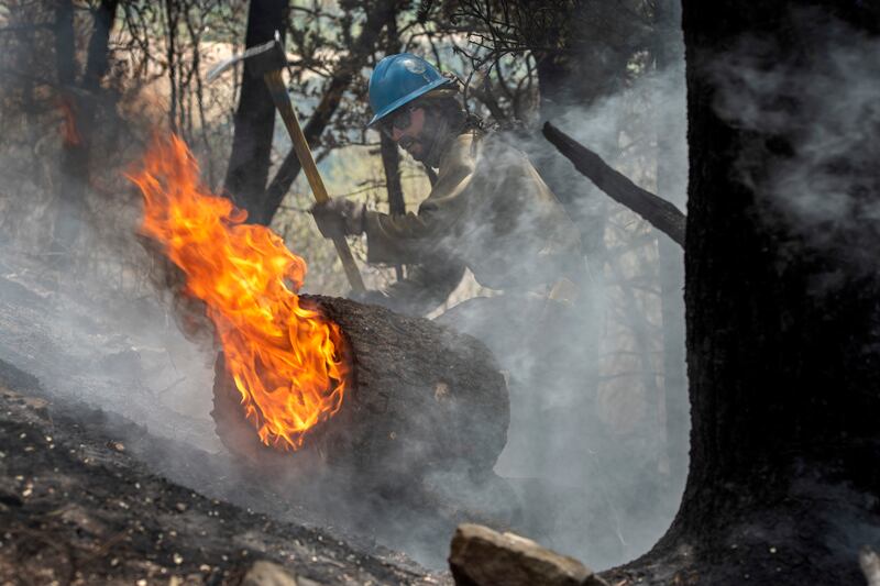 Tyler Freeman digs a hole to keep a burning log from rolling down a slope in the Carson National Forest west of Chacon, N.M.