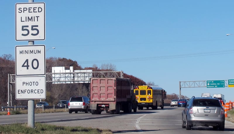 A speed limit sign on a busy highway with a sign below it reading “photo enforced.”