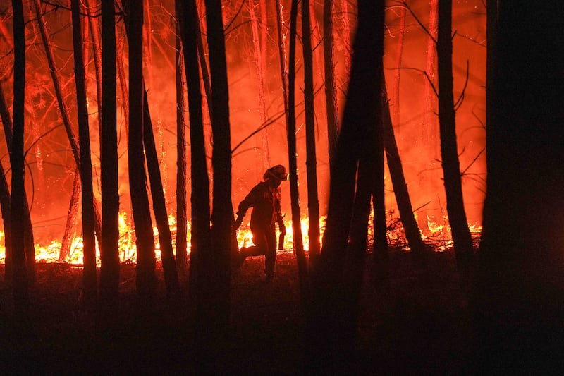 A firefighter is silhouetted against a fire burning outside a village.