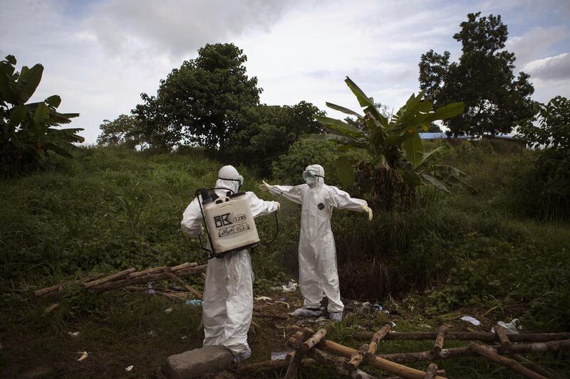 FILE - In this Sept. 24, 2014, file photo, a health worker sprays a colleague with disinfectant after working inside a morgue with people suspected of dying from the Ebola virus, in Kenema, eastern Sierra Leone. An Associated Press investigation found tha