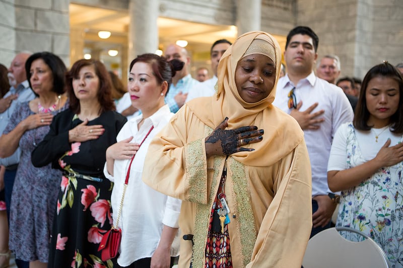 Zainab Abdi of Somalia and others stand for the national anthem during a nationalization ceremony at the Utah State Capitol in Salt Lake City on Friday, Aug. 3, 2018. Citizenship was conferred on 110 people from 41 countries.