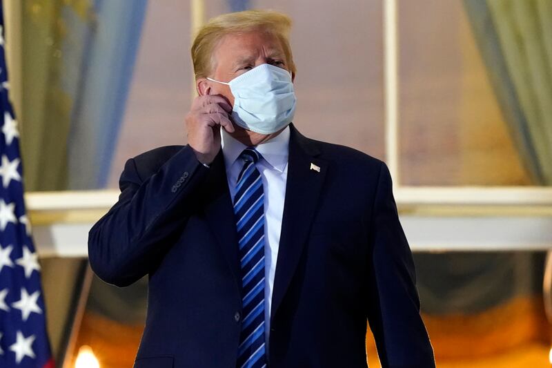 President Donald Trump removes his mask as he stands on the balcony outside of the Blue Room as he returns to the White House Monday, Oct. 5, 2020, in Washington, after leaving Walter Reed National Military Medical Center, in Bethesda, Md. Trump announced he tested positive for COVID-19 on Oct. 2.
