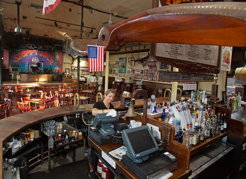 In this photo provided by the Florida Keys News Bureau, Becky Lawrence sanitizes a point of sale system at Sloppy Joe’s Bar, Tuesday, March 17, 2020, in Key West, Fla. The iconic watering hole, a frequent hangout of the late writer Ernest Hemingway, was void of customers Tuesday evening as it joined other bars around Florida that closed under a state declaration signed by Gov. Ron DeSantis to help curb the spread of the new coronavirus. (Carol Tedesco/Florida Keys News Bureau via AP)