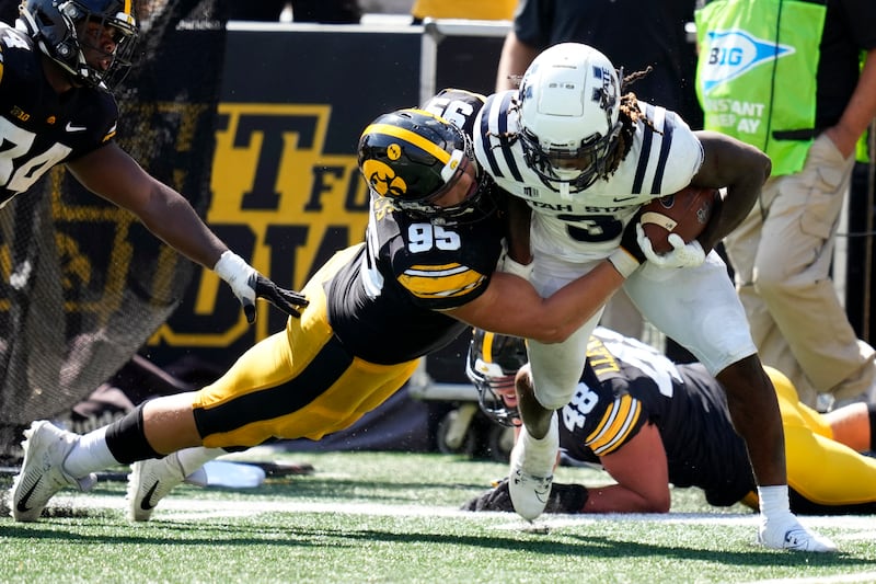 Utah State running back Rahsul Faison (wearing white) tries to break a tackle by Iowa defensive lineman Aaron Graves