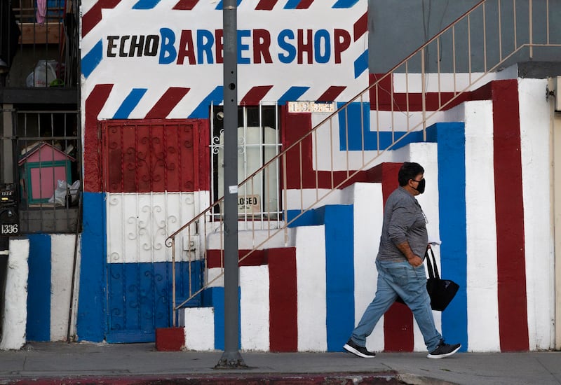 In this Friday May 8, 2020 file photo A pedestrian wears a mask as he walks past the closed Echo Barber Shop in the Echo Park neighborhood of Los Angeles
